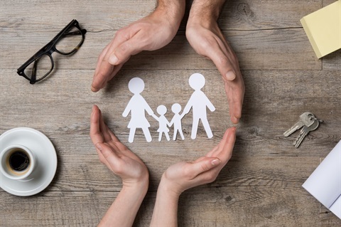 Two pairs of hands around a paper cutout of a family.
