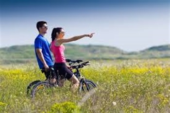 Couple bike riding in field of yellow flowers
